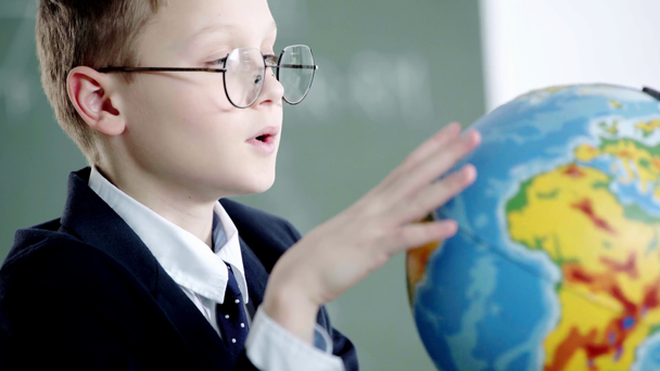 školák v brýlích ukazujícími prstem na glóbu a s úsměvem ve škole  - Záběry, video