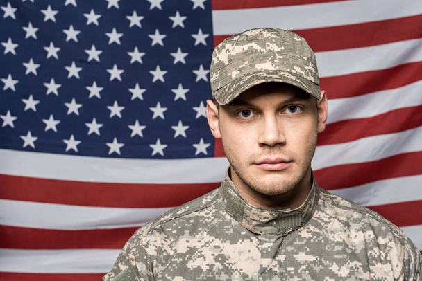 bel soldato in uniforme militare e cappello guardando la fotocamera vicino alla bandiera dell'America
 - Foto, immagini