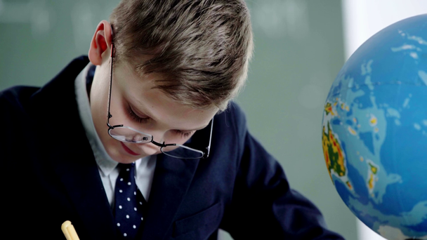 school jongen in glazen kijken naar Globe terwijl het houden van potlood in klas  - Video