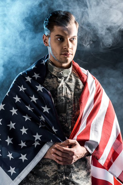 soldier in military uniform with clenched hands and american flag on black with smoke - Foto, imagen