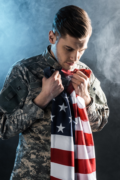 upset soldier holding american flag on black with smoke  - Foto, Bild