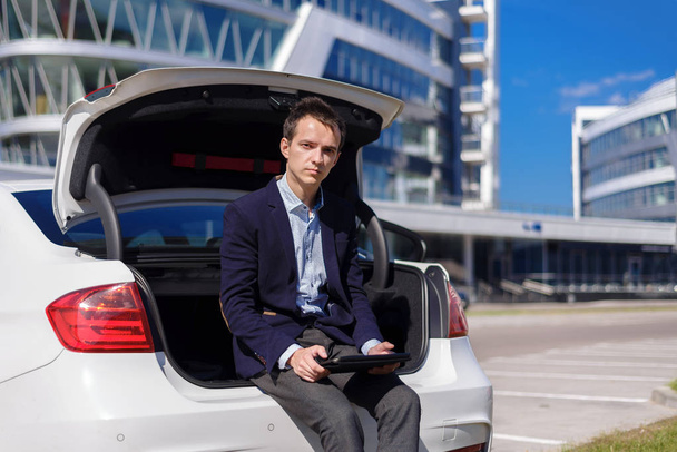 successful young businessman freelancer working outside in the city. man sit on car boot with tablet  - Fotografie, Obrázek