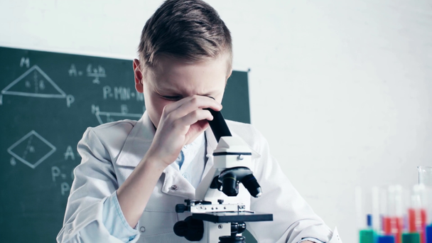 επιλεκτική εστίαση της γραφής των παιδιών και κοιτάζοντας μέσα από το μικροσκόπιο κοντά σε δοκιμαστικούς σωλήνες με υγρό στην τάξη  - Πλάνα, βίντεο