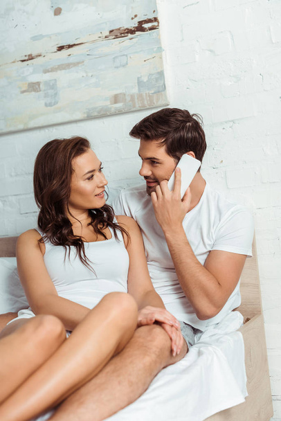 gelukkige man glimlachend in de buurt van aantrekkelijke vriendin tijdens het praten op de smartphone  - Foto, afbeelding