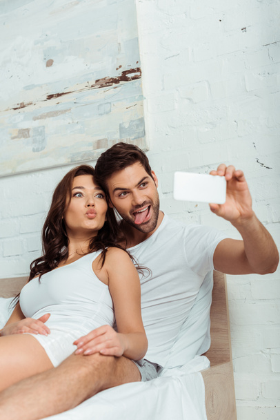 felice uomo mostrando lingua vicino attraente ragazza con anatra faccia mentre prende selfie
  - Foto, immagini