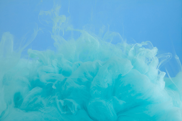 Nahaufnahme von türkisfarbener Aquarellfarbe wirbelt vereinzelt auf blau - Foto, Bild