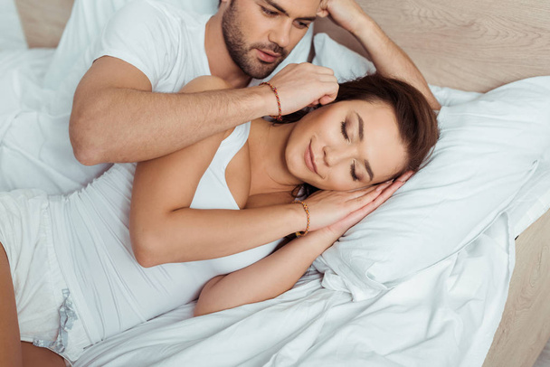 Красивый мужчина трогает привлекательную женщину лежащую на кровати с закрытыми глазами
  - Фото, изображение