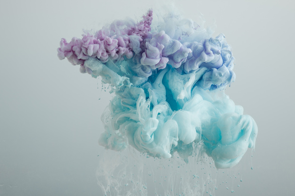Close up view of light blue, pink and purple paint mixing isolated on grey - 写真・画像