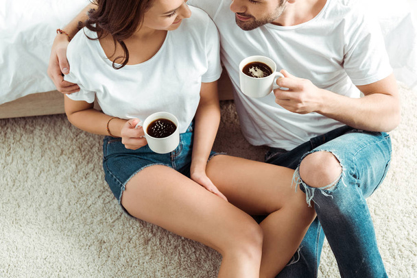 overhead view of happy man sitting with cheerful girl and holding cup in bedroom  - Foto, Imagem