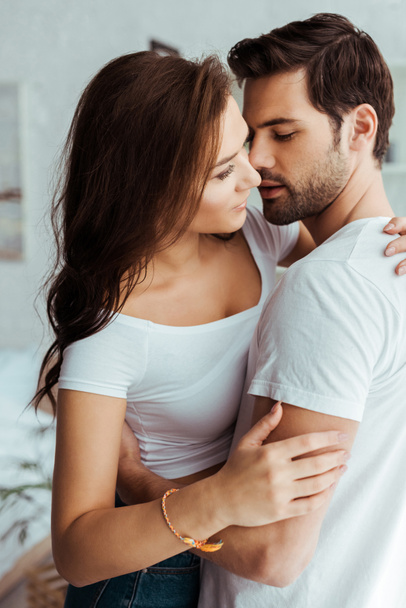 przystojny mężczyzna przytulanie i patrząc na atrakcyjną dziewczynę w białym t-shirt  - Zdjęcie, obraz