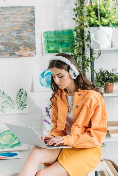 attentive girl in headphones using laptop while sitting on desk at home - 写真・画像