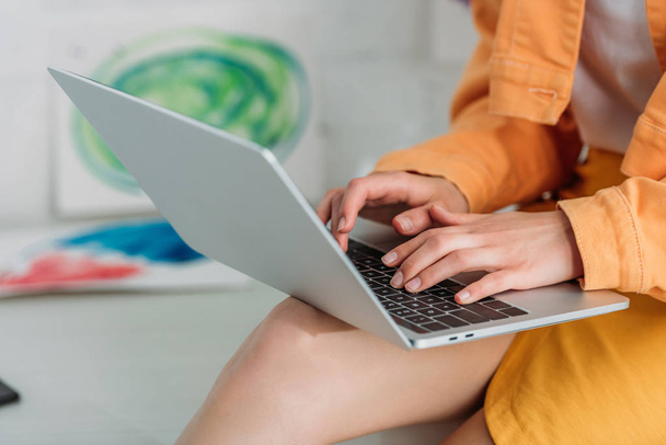 partial view of young woman in orange clothing using laptop at home  - Photo, Image