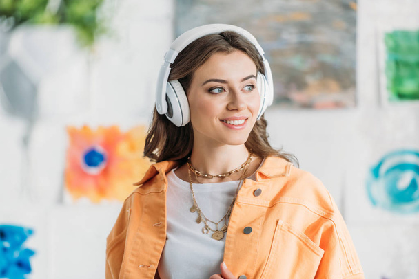 модна молода жінка в намисті слухає музику в навушниках і дивиться в сторону
 - Фото, зображення