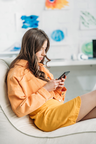 concentrated young woman in orange closing using smartphone at home - Foto, Imagen