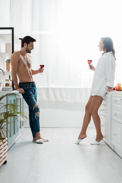 handsome shirtless man and attractive brunette girl holding wine glasses in modern kitchen  - Foto, immagini