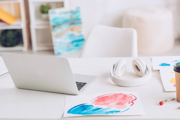 ordinateur portable, écouteurs et peintures sur table blanche près de paiments colorés
 - Photo, image