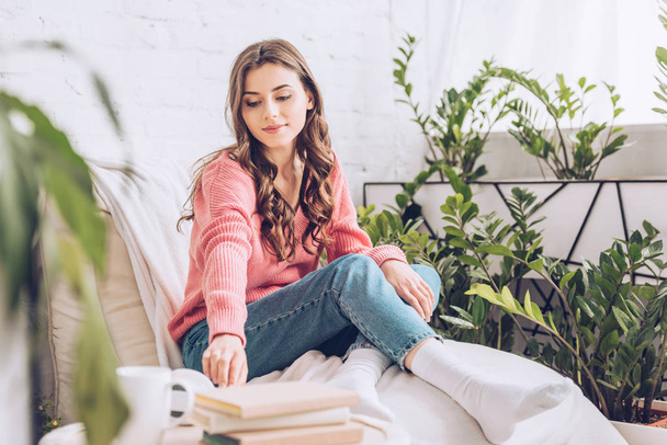 selektivní zaměření atraktivní dívky, která si bere knihu, zatímco sedí doma ve společenské místnosti s bílým kočár - Fotografie, Obrázek