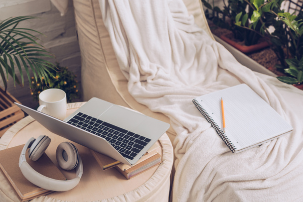 ноутбук, навушники, книги та чашка кави на пуфі біля м'якого шезлонг-залу
 - Фото, зображення