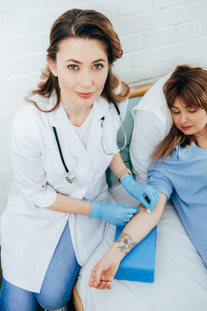 Arzt in Latexhandschuhen bereitet Spender auf Blutspende vor - Foto, Bild