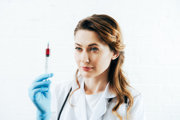 doctor in white coat holding syringe with blood sample on white - Фото, изображение