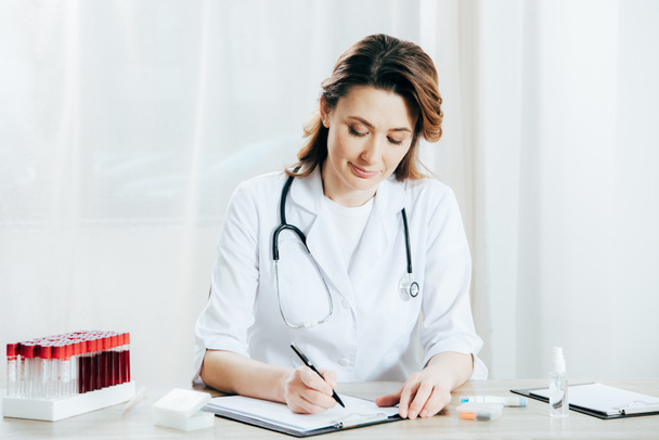 doctor in white coat writing on clipboard in clinic - Photo, Image