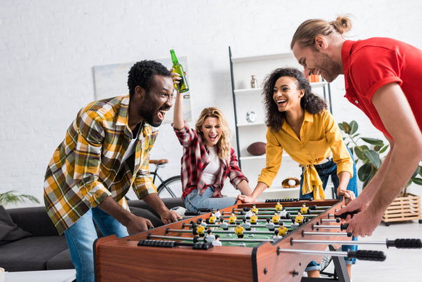 Four happy and joyful multiethnic friends playing table football in living room - Foto, Bild