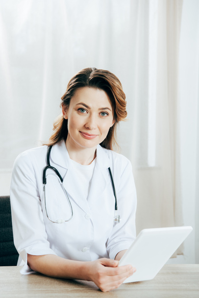 médecin souriant en manteau blanc avec stéthoscope en utilisant une tablette numérique en clinique
 - Photo, image