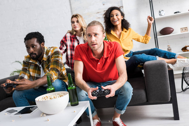 selective focus of multicultural men playing video game near girls at home - Фото, изображение