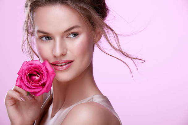 πορτρέτο της ελκυστική νεαρή γυναίκα με ροζ τριαντάφυλλο που ποζάρει σε ροζ φόντο - Φωτογραφία, εικόνα