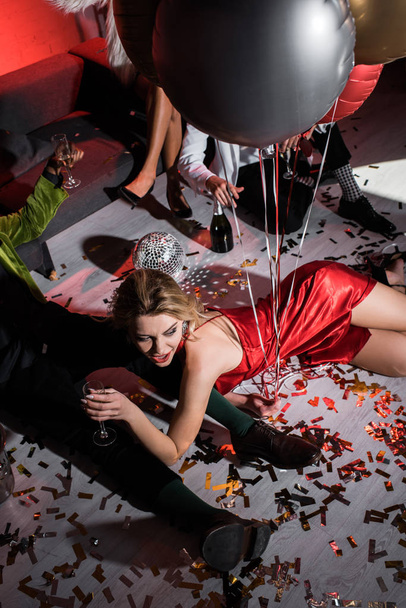 bovenaanzicht van Happy Girl Holding ballonnen terwijl liggend op de vloer in de buurt van vrienden  - Foto, afbeelding