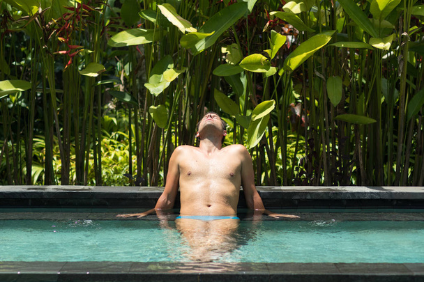 Мужчина расслабляется в открытом спа-бескрайнем бассейне в окружении пышной тропической зелени Убуда, Бали
. - Фото, изображение