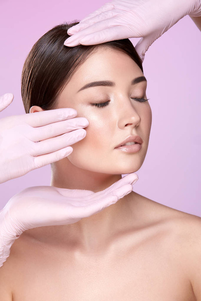 Teilansicht von Kosmetikerinnen in Gummihandschuhen und jungen brünetten Frauen auf rosa Hintergrund - Foto, Bild