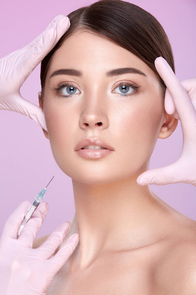 partial view of cosmetologists in rubber gloves and young brunette woman on pink background - Foto, Imagem