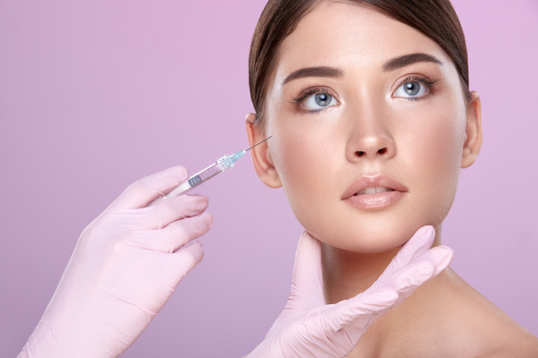 partial view of cosmetologist in rubber gloves with syringe and young brunette woman on pink background - Foto, immagini
