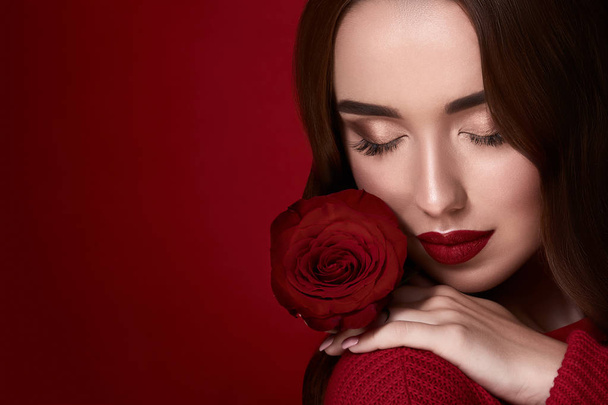 attraktive junge Frau mit Abendschminke und roter Rose auf rotem Hintergrund - Foto, Bild