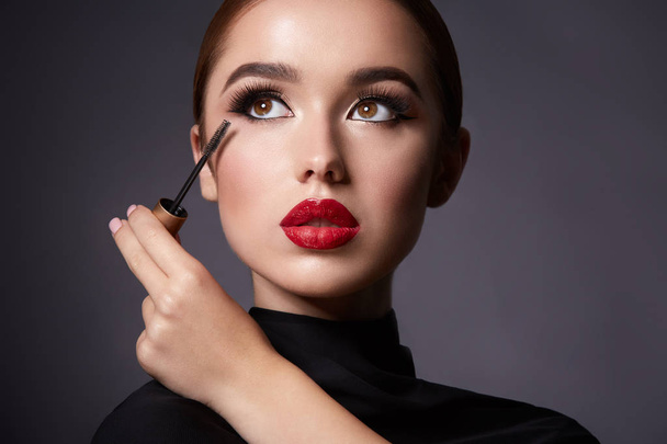 aantrekkelijke jonge vrouw met avond make-up en mascara op donkere achtergrond - Foto, afbeelding