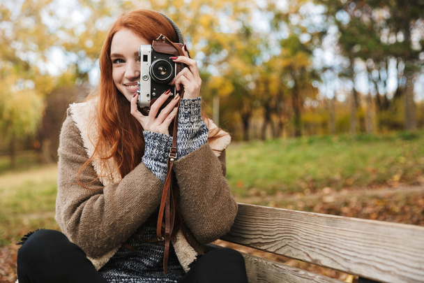 Lovely redheaded young girl listening to music, holding photo camera - Fotografie, Obrázek