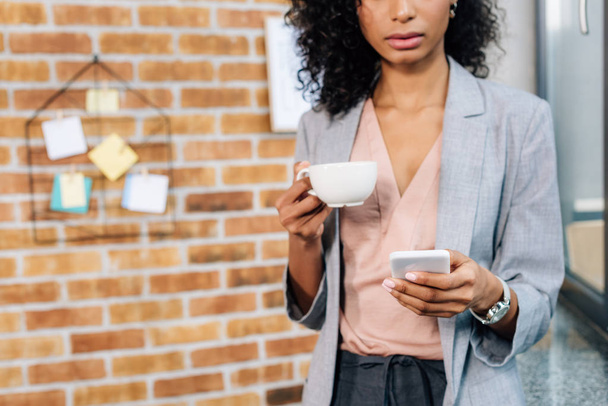 Cropped view of african american Casual businesswoman with coffee cup using smartphone - Photo, Image