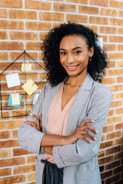 sonriente afroamericana Casual mujer de negocios con los brazos cruzados en la oficina loft
 - Foto, imagen