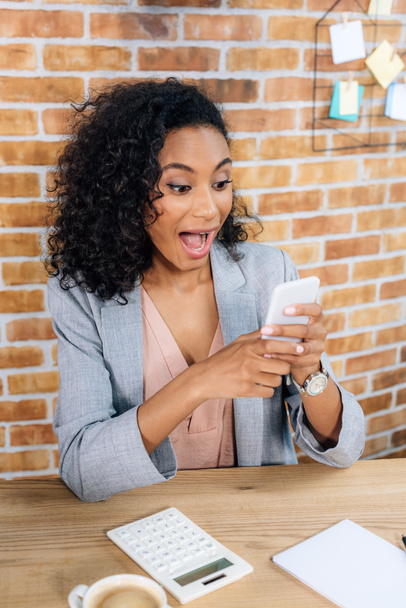 excited african american Casual businesswoman using smartphone at desk - Foto, Imagen