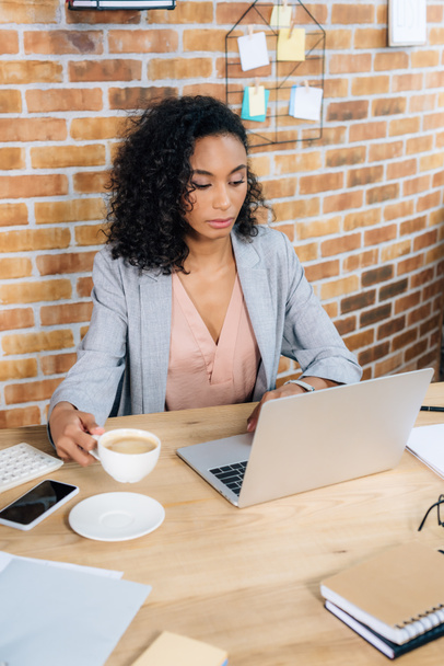 african american Casual businesswoman with coffee cup using laptop at office desk - Photo, Image