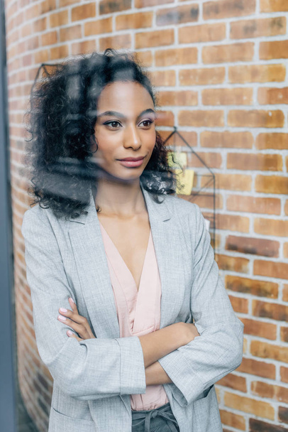 african american Casual businesswoman with crossed arms looking through window in loft office - Foto, Imagem