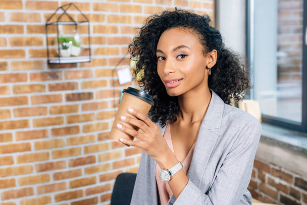 beautiful african american Casual businesswoman with coffee to go looking at camera in office - 写真・画像