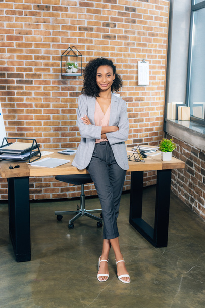 smiling african american Casual businesswoman with crossed arms near desk in office - Photo, Image