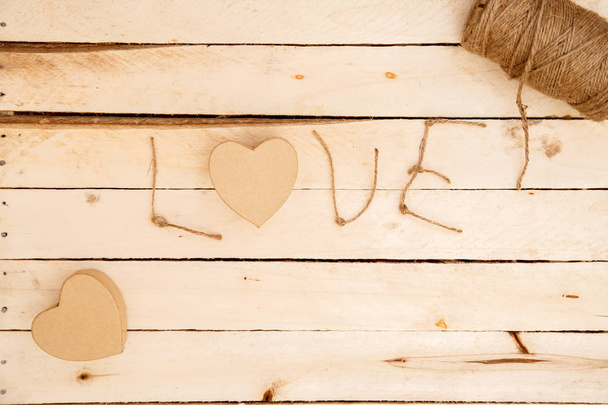vrouwenhanden verspreiden harten en het woord liefde voor draden op een lichte houten achtergrond. het uitzicht vanaf de top - Foto, afbeelding