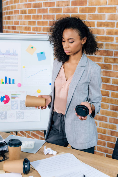 african american Casual businesswoman holding coffee to go near flipchart in loft office - Фото, изображение