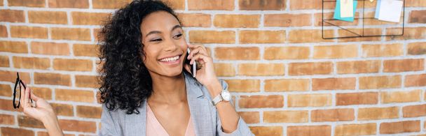 Panoramaaufnahme einer lächelnden afrikanisch-amerikanischen Gelegenheitsunternehmerin, die mit dem Smartphone spricht - Foto, Bild