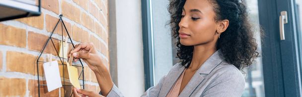 plano panorámico de la mujer de negocios afroamericana casual colgando notas adhesivas con alfileres en la oficina loft
 - Foto, imagen