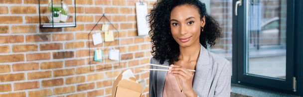 panoramic shot of african american Casual businesswoman with takeaway box and chopsticks in office - 写真・画像