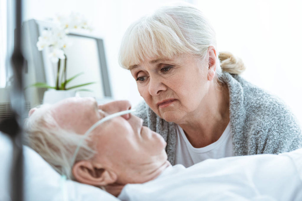 smutna Starsza kobieta patrzy na męża w śpiączce w klinice - Zdjęcie, obraz